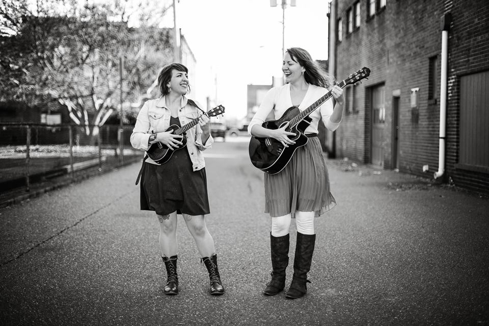 Two women, one with guitar and one with ukulele.