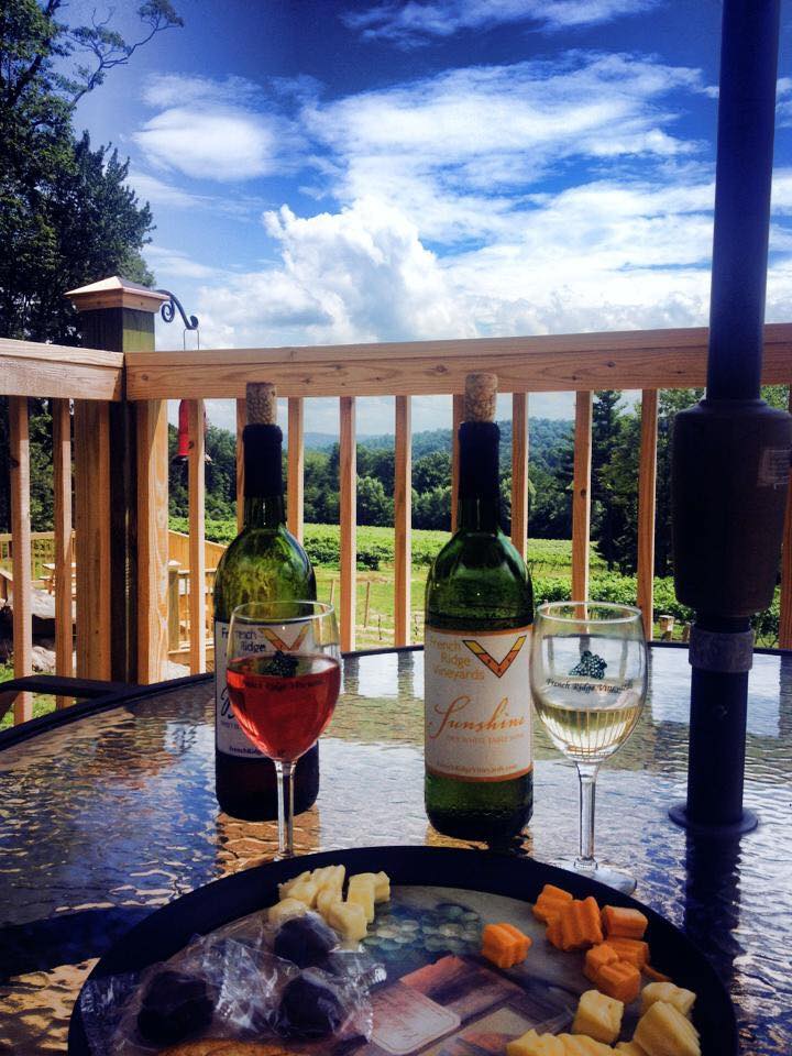 Two French Ridge wine bottles, filled glasses and a cheese plate on a table overlooking a vineyard.